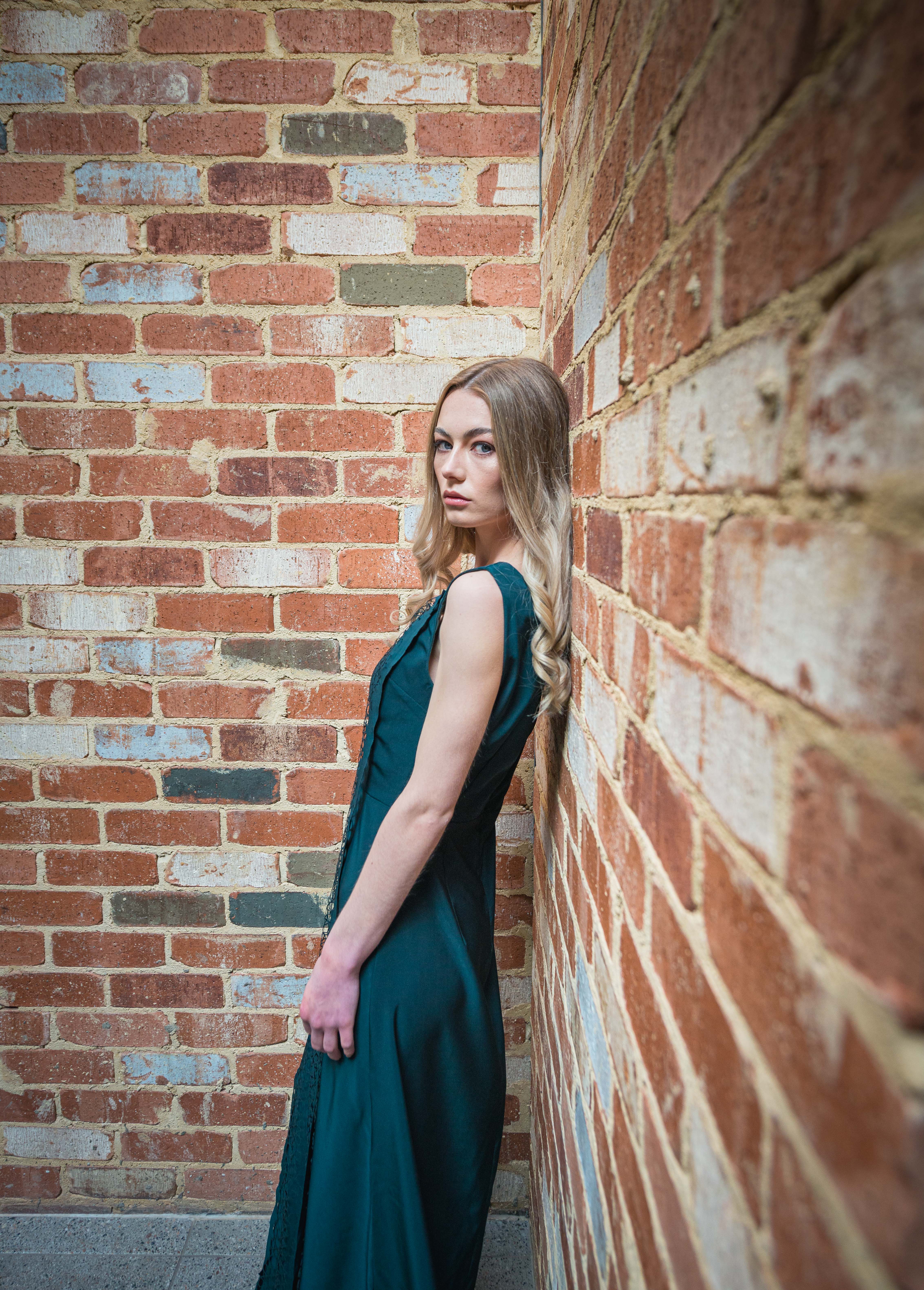 Finesse Model 1 leaning against a brick wall with long green dress